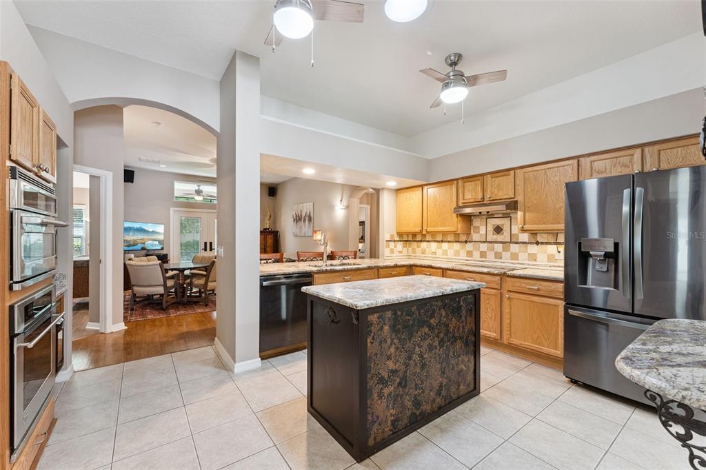 A kitchen features oak cabinets, granite countertops, a dark wood island, and stainless steel appliances — 293 KETTERING ROAD, DELTONA, FL