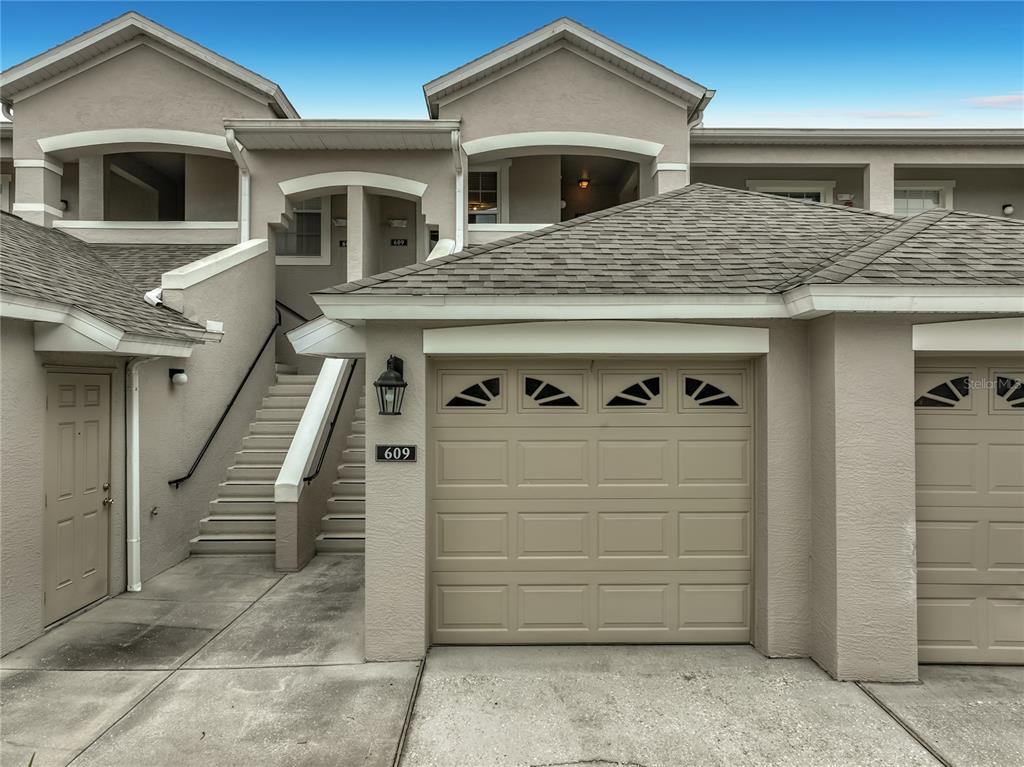 A two-story townhouse exterior features a beige garage, a concrete driveway, and an outdoor staircase — 9417 MYRTLE CREEK LANE UNIT 609, ORLANDO, FL