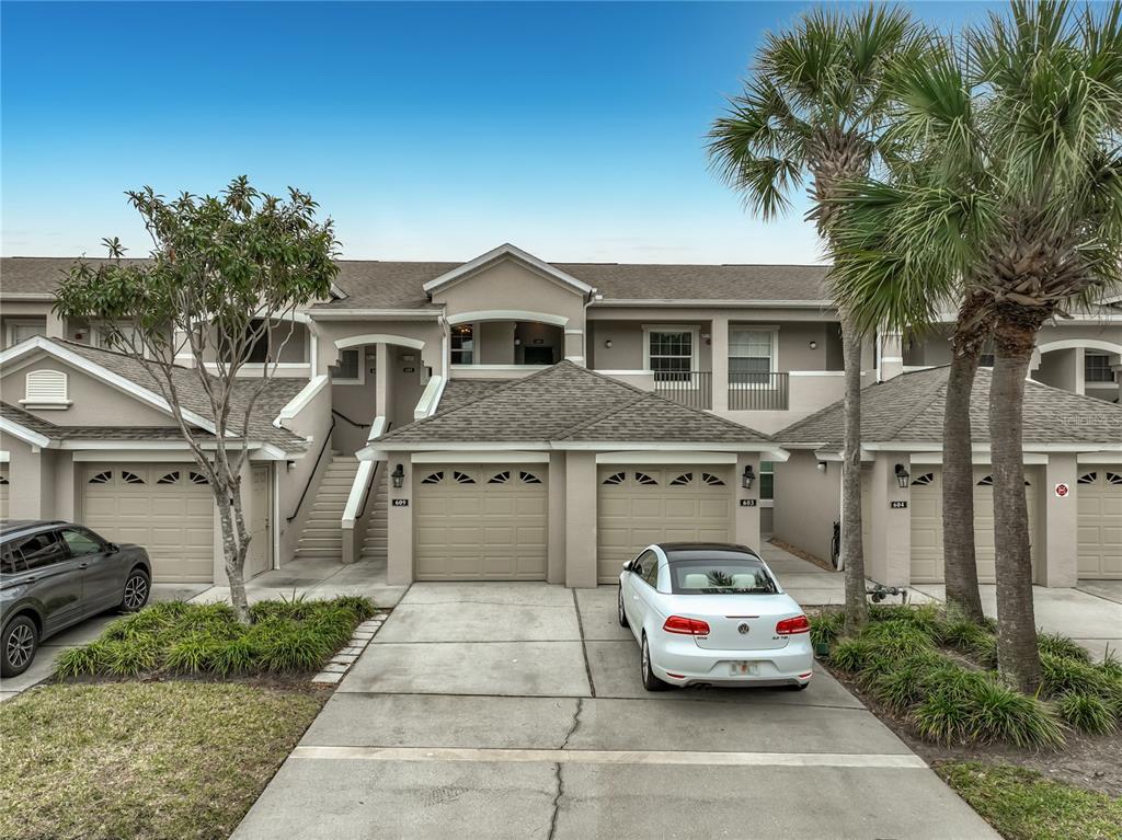 The exterior of a multi-unit residential building features tan stucco, garage doors, and palm trees — 9417 MYRTLE CREEK LANE UNIT 609, ORLANDO, FL