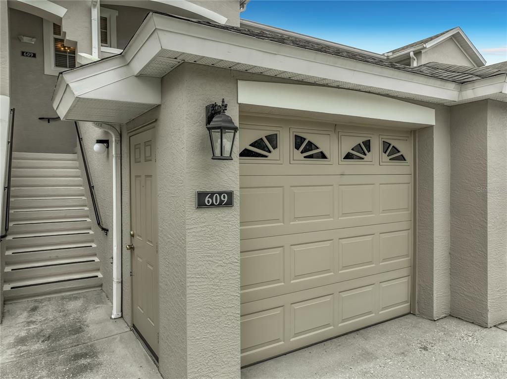 A beige garage door and a side entry door are located next to an outdoor staircase — 9417 MYRTLE CREEK LANE UNIT 609, ORLANDO, FL