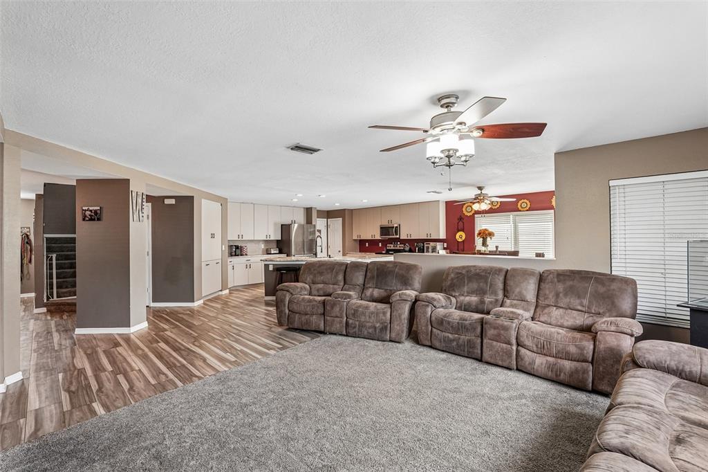 A spacious living room with gray carpet opens to a kitchen with light-colored cabinetry — 2279 MISTLETO LANE, NORTH PORT, FL