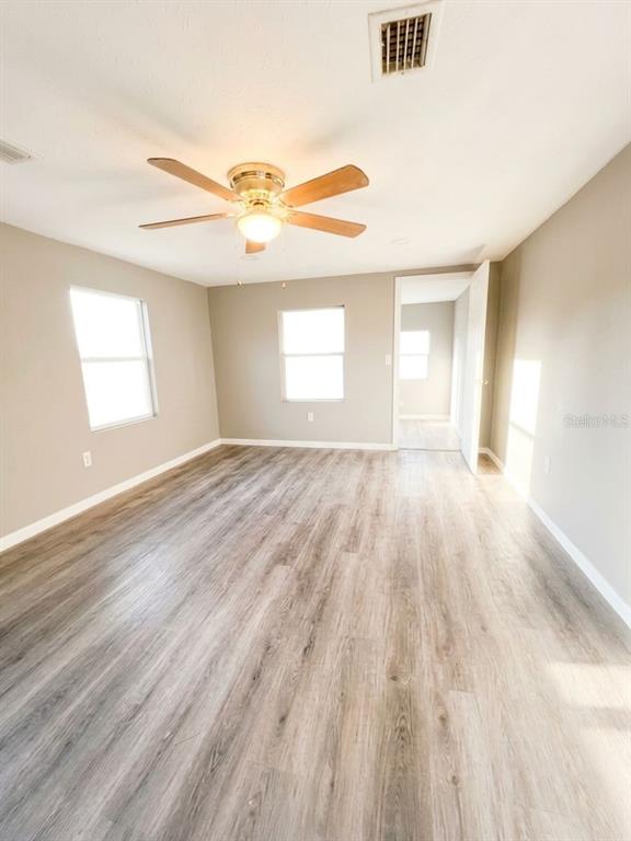 An empty room features light wood-look flooring, beige walls, and a ceiling fan — 3420 AVENUE R NW, WINTER HAVEN, FL