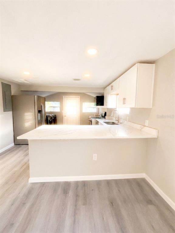 A kitchen features white cabinets, a marble-look peninsula countertop, and light-colored wood-style flooring — 3420 AVENUE R NW, WINTER HAVEN, FL