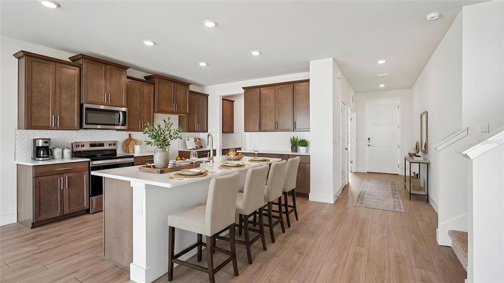 A modern kitchen features wood cabinets, a white island with bar stools, and hardwood floors — 11225 DUCKLING WAY, WEEKI WACHEE, FL