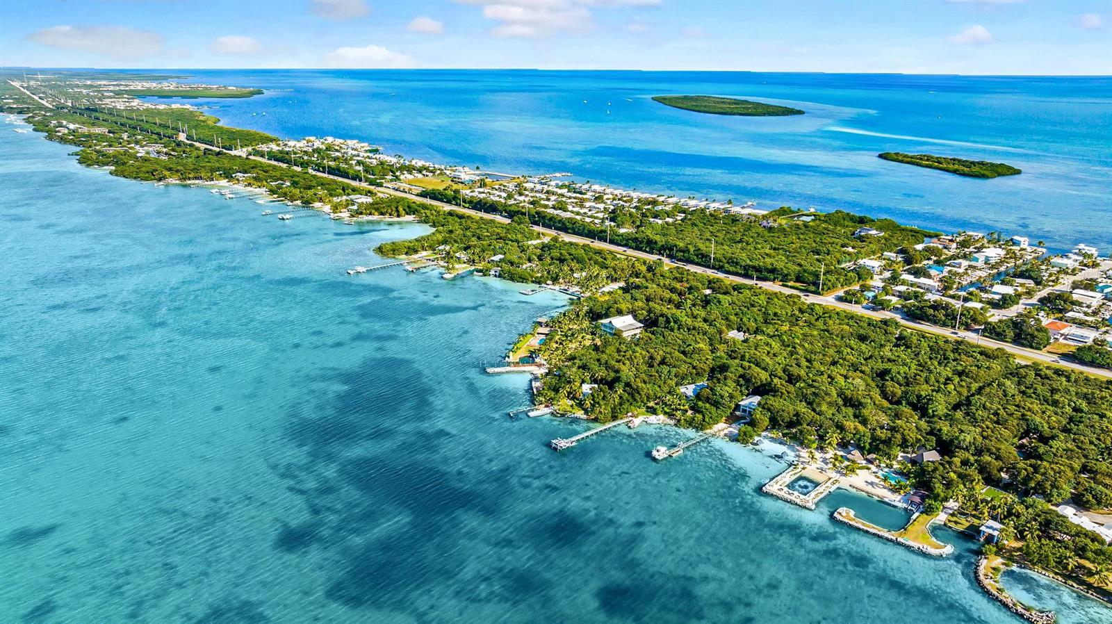 An aerial view shows a narrow, tree-covered island surrounded by turquoise water and a highway — 95410 Overseas Highway, Key Largo FL 33037, KEY LARGO, FL