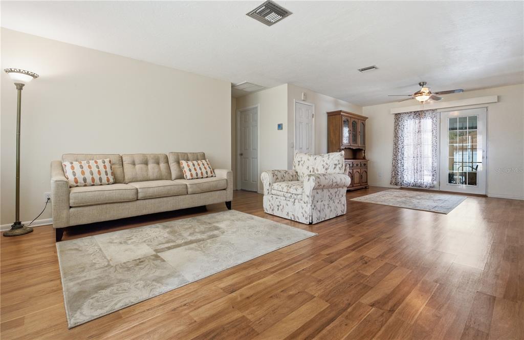 A living room with wood flooring, a beige sofa, a floral armchair, and glass doors — 527 BOUNTY AVENUE NE, PALM BAY, FL