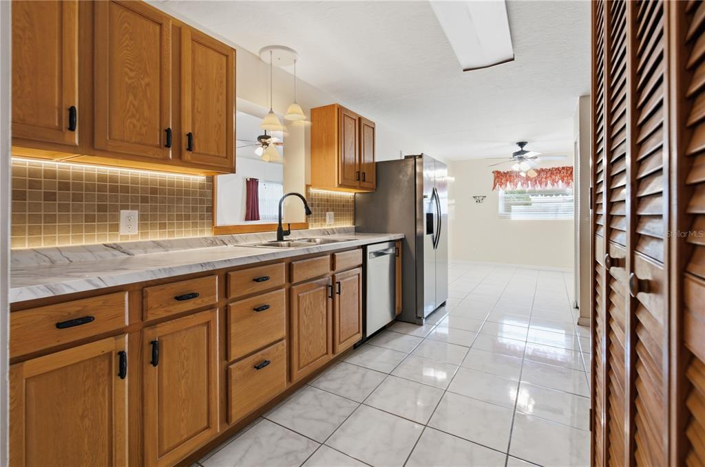 A kitchen features oak cabinets, white marble-look countertops, a tiled backsplash, and light-colored floor tiles — 527 BOUNTY AVENUE NE, PALM BAY, FL