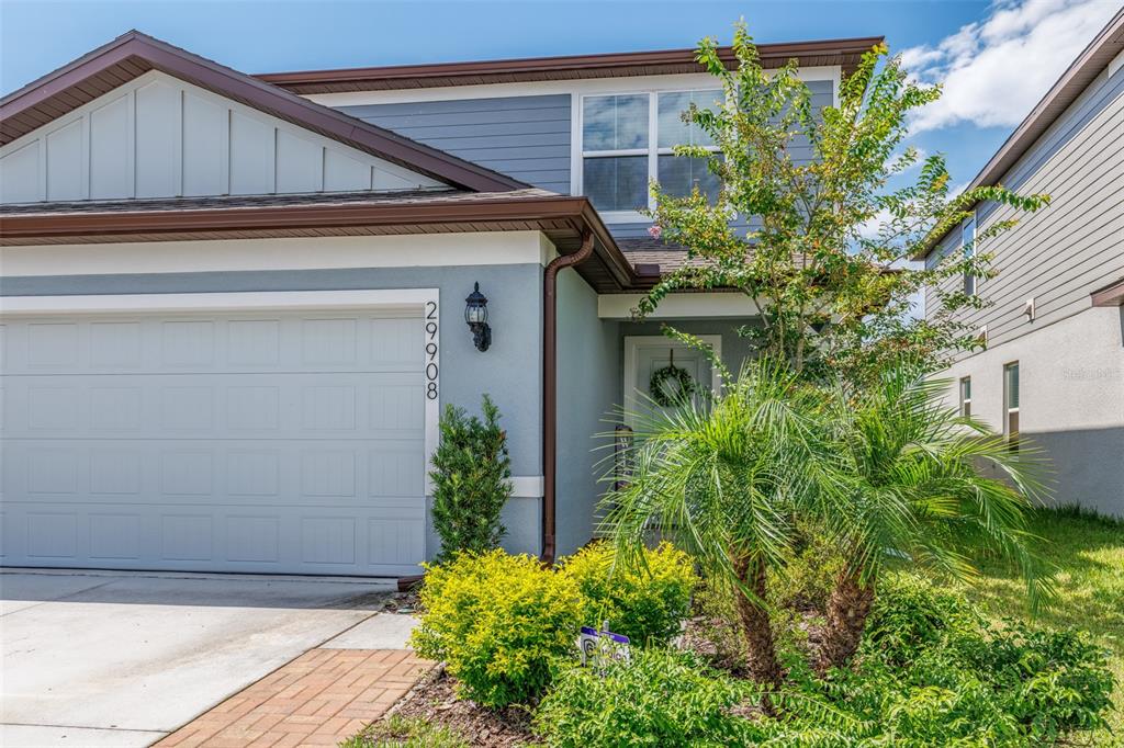 A two-story house features a gray garage, a front entrance, and landscaping under a blue sky — 29908 MARQUETTE AVENUE, WESLEY CHAPEL, FL