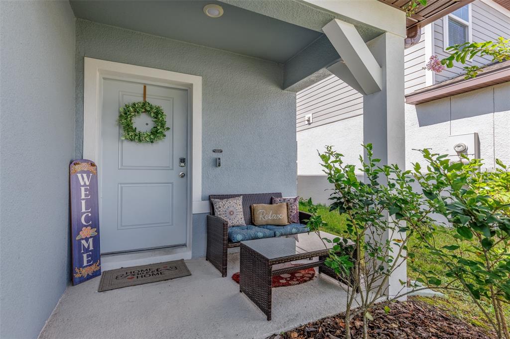 A covered front porch features a light blue door, a wicker bench, and a small table — 29908 MARQUETTE AVENUE, WESLEY CHAPEL, FL