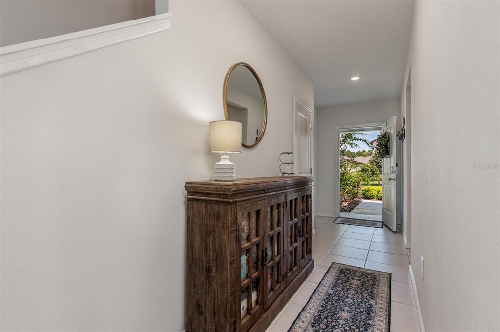 A tiled entryway features a wooden console table, a lamp, a mirror, and an open door — 29908 MARQUETTE AVENUE, WESLEY CHAPEL, FL