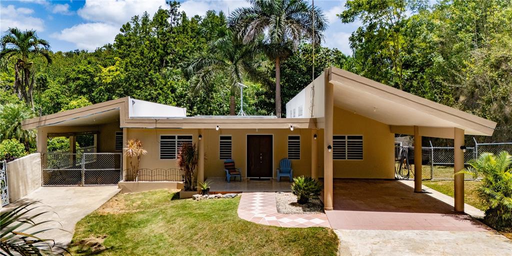 A single-story house with a carport and a tiled walkway sits before a lush forest — Comm Cienguetas #33 BO ESPERANZA, ARECIBO, PR