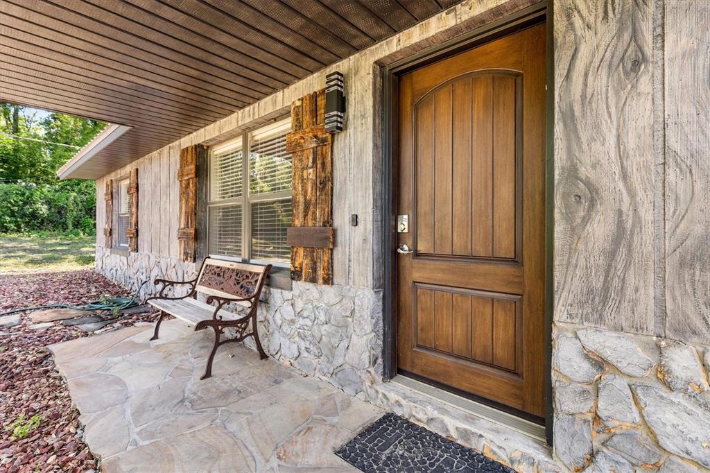 A stone-accented porch features a wooden front door, a metal bench, and rustic shutters — 37149 GRAYS AIRPORT ROAD, LADY LAKE, FL