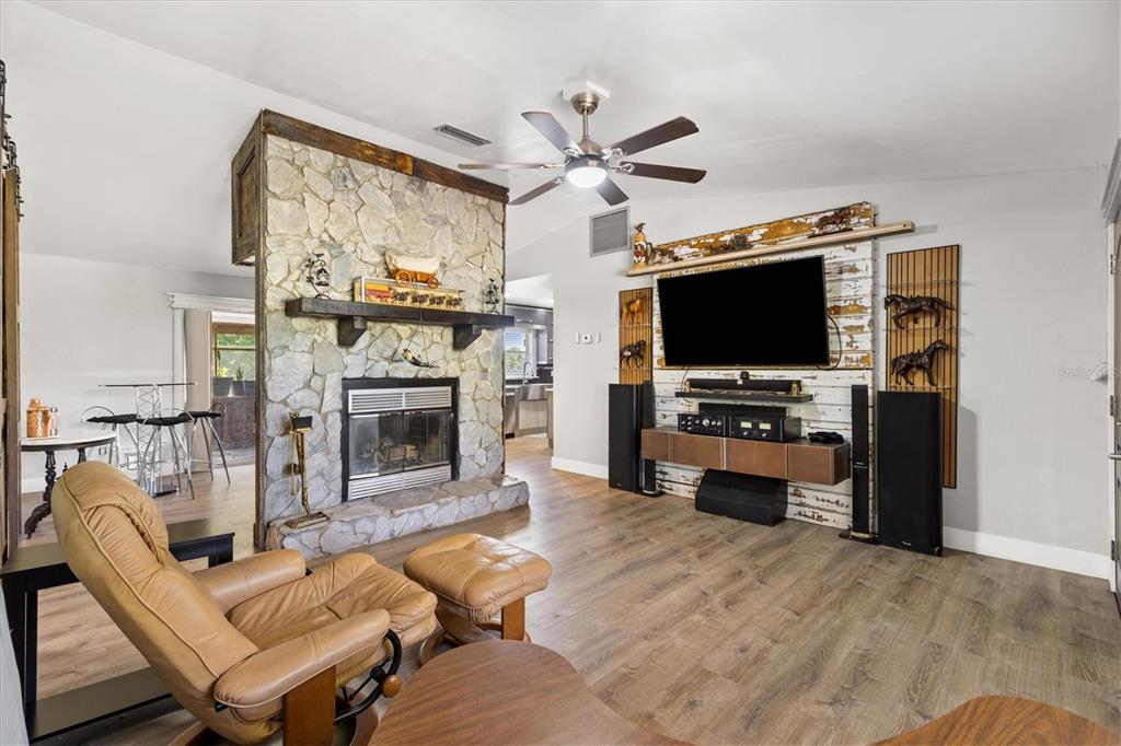 A living room features a stone fireplace, a wall-mounted television, and wood-look flooring — 37149 GRAYS AIRPORT ROAD, LADY LAKE, FL