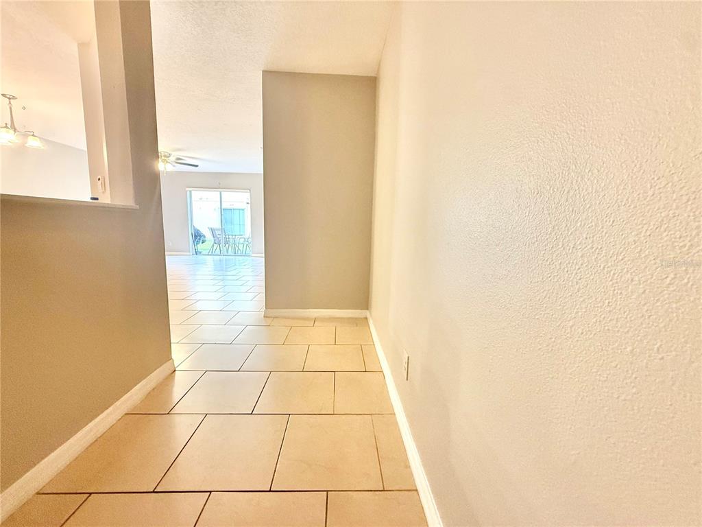 A hallway with beige tile flooring leads toward a living area with a sliding glass door — 609 CRESTING OAK CIRCLE UNIT 98, ORLANDO, FL