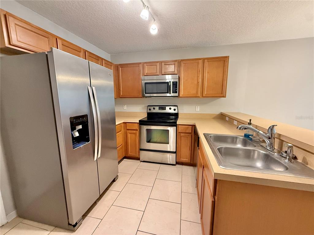 A kitchen features stainless steel appliances, light wood cabinets, and beige tile flooring — 609 CRESTING OAK CIRCLE UNIT 98, ORLANDO, FL