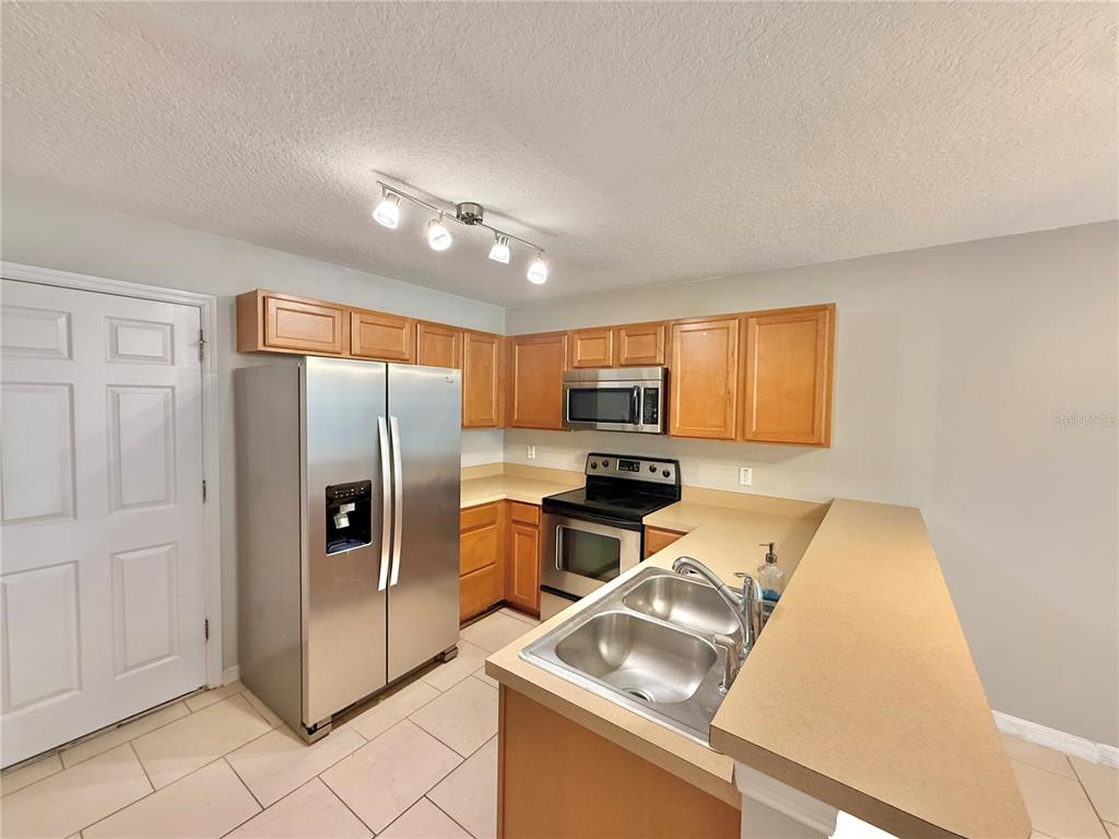 A kitchen features light wood cabinets, stainless steel appliances, a double sink, and tile flooring — 609 CRESTING OAK CIRCLE UNIT 98, ORLANDO, FL