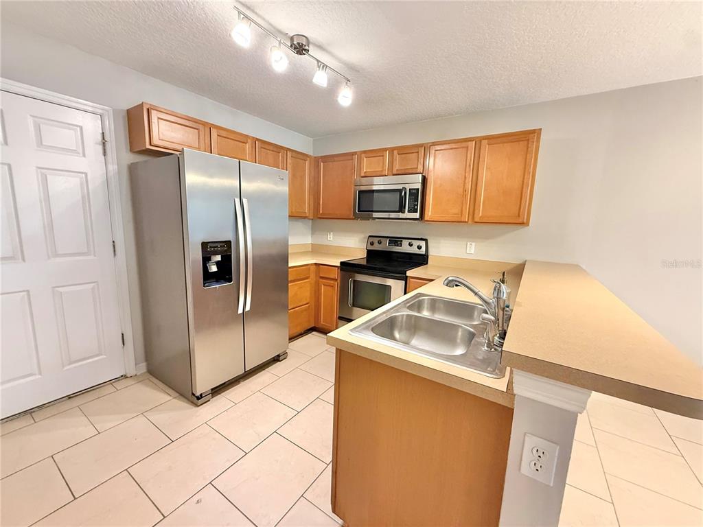 A kitchen features wood cabinets, stainless steel appliances, a double sink, and tile flooring — 609 CRESTING OAK CIRCLE UNIT 98, ORLANDO, FL