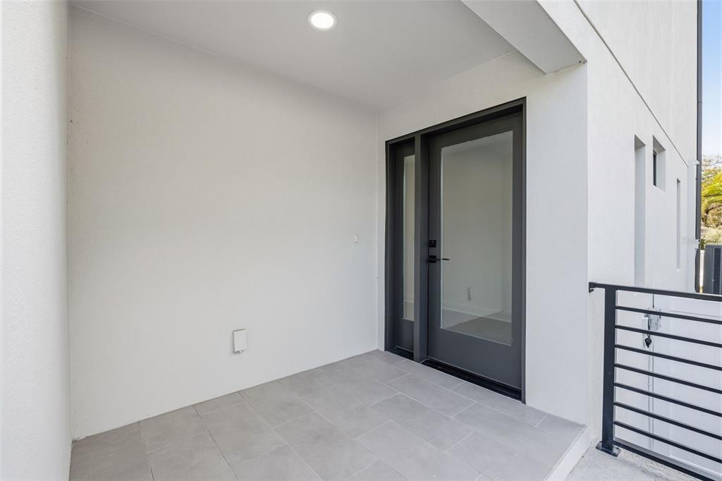 A covered balcony features gray tiled flooring, a glass-paneled door, and a black metal railing — 4509 W NORTH A STREET UNIT 1, TAMPA, FL