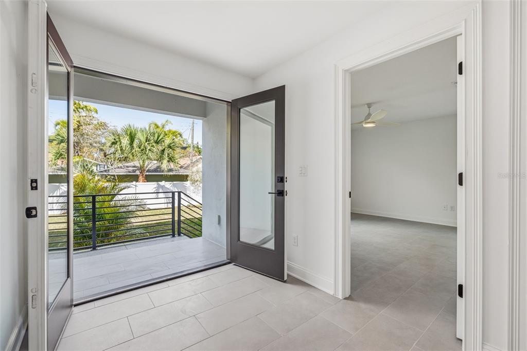 A room with light tile flooring leads to an outdoor balcony through a glass door — 4509 W NORTH A STREET UNIT 1, TAMPA, FL