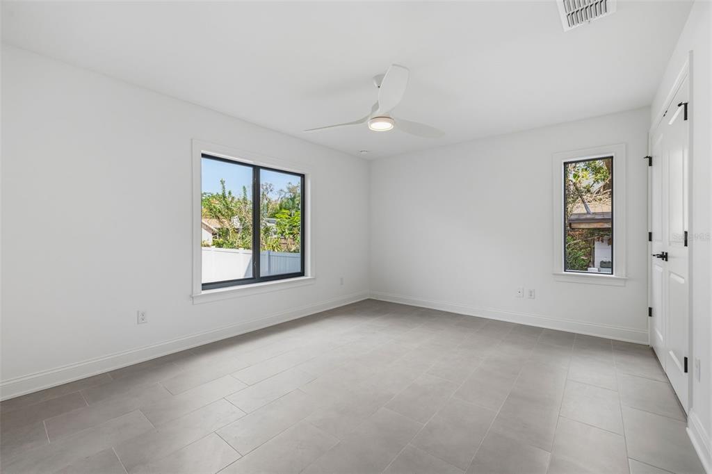 A bright, empty bedroom features white walls, gray tile flooring, a ceiling fan, and windows — 4509 W NORTH A STREET UNIT 1, TAMPA, FL