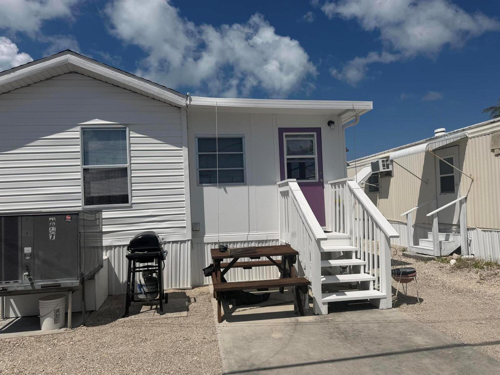 A white mobile home exterior features a purple door, wooden picnic table, and outdoor grill — 1361 Overseas Highway # G15, Marathon FL 33050, MARATHON, FL
