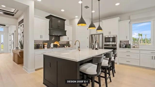 A modern kitchen features a dark island with bar stools, white cabinetry, and pendant lighting — 13032 CAMELOT LANE, PUNTA GORDA, FL