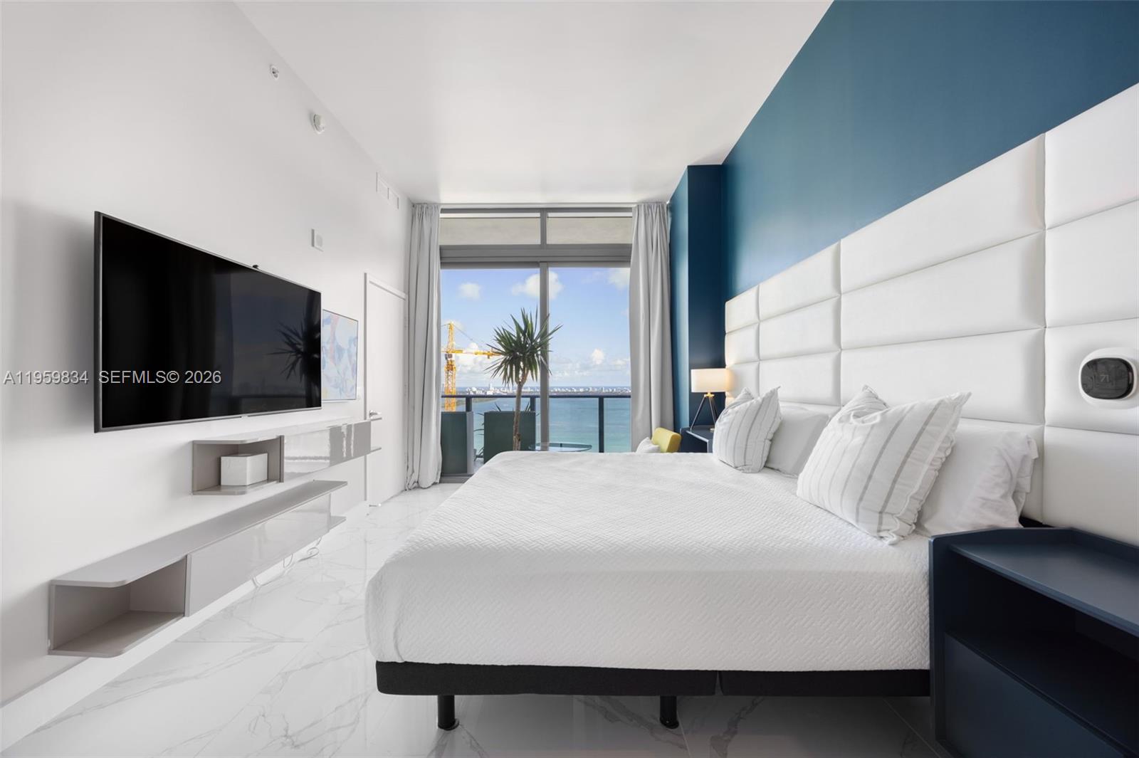A modern bedroom features a white tufted headboard, blue accent wall, and a balcony view — 460 NE 28th St # 4002, Miami FL 33137, MIAMI, FL