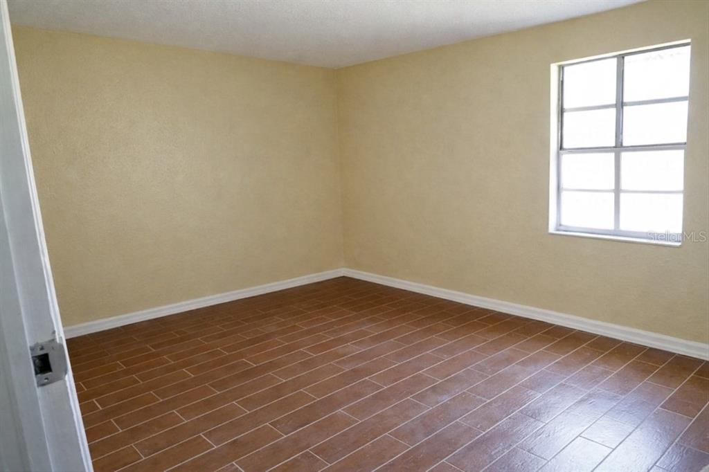 An empty room with tan walls, white trim, and brown wood-look tile flooring — 1709 E IDELL STREET UNIT B, TAMPA, FL