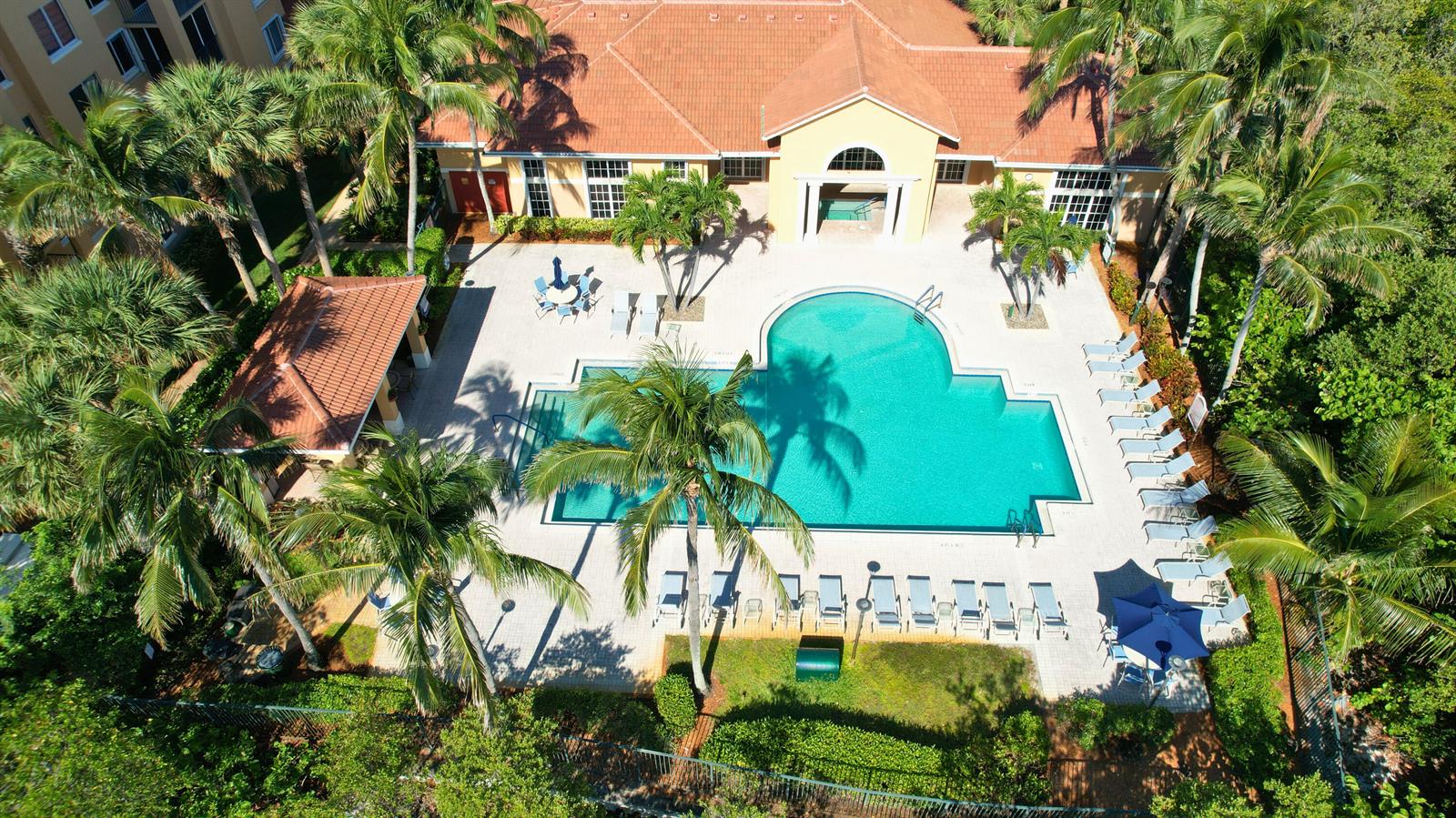 An aerial view shows a swimming pool with lounge chairs and a clubhouse with palm trees — 800 Scotia Drive # 203, Hypoluxo FL 33462, HYPOLUXO, FL