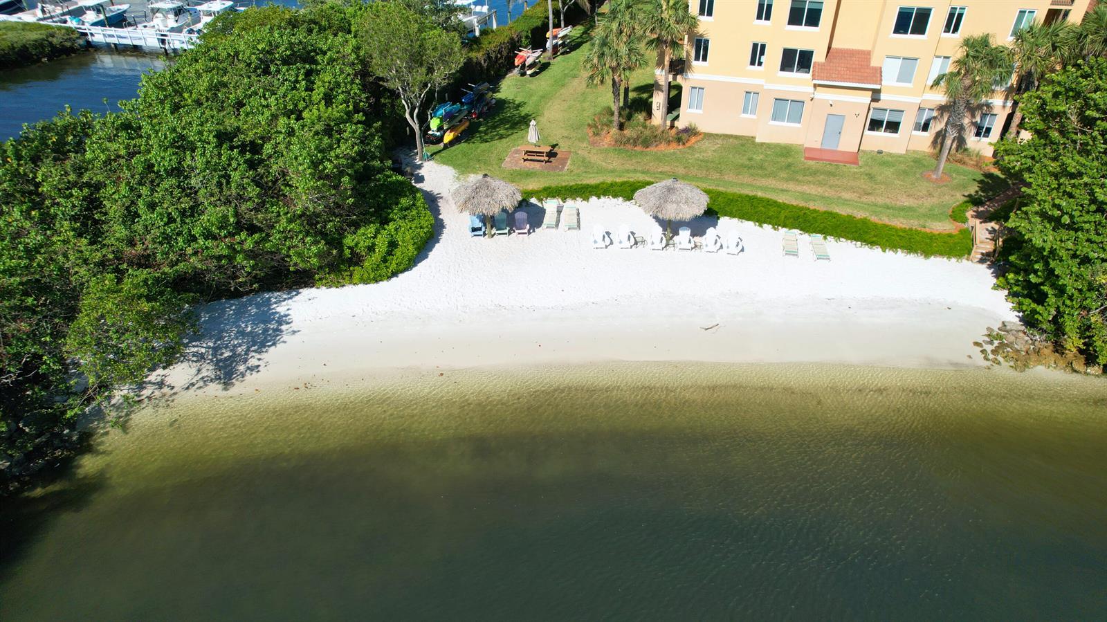 An aerial view shows a sandy beach area with tiki umbrellas next to a building — 800 Scotia Drive # 203, Hypoluxo FL 33462, HYPOLUXO, FL