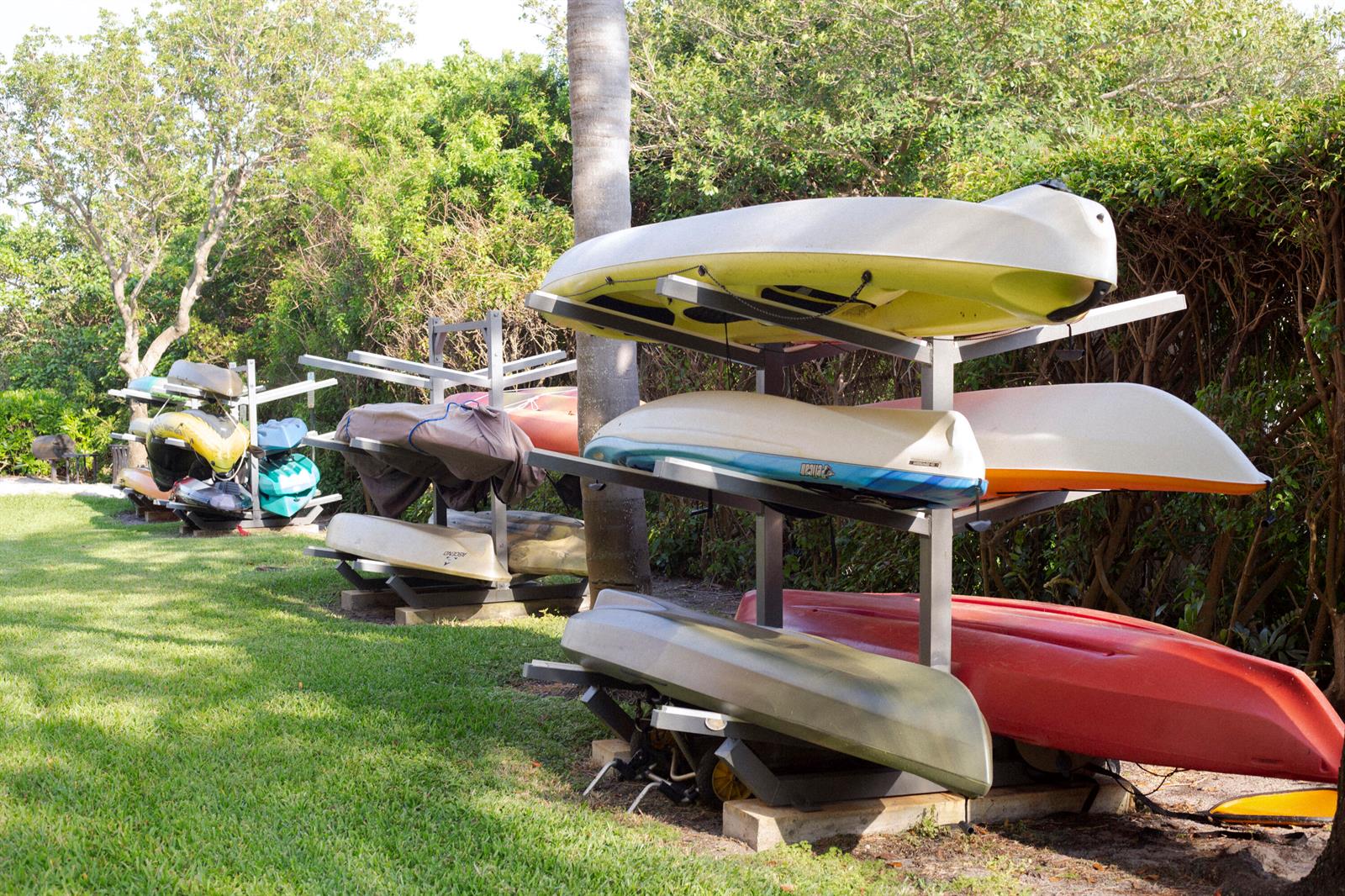 Multiple kayaks are stored on metal racks in a grassy area near trees — 800 Scotia Drive # 203, Hypoluxo FL 33462, HYPOLUXO, FL