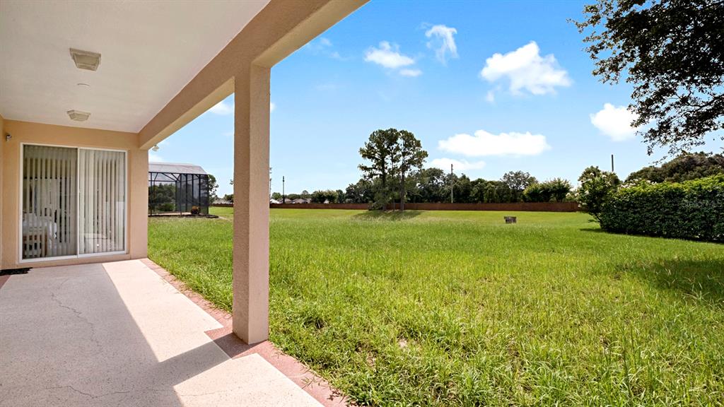 A covered concrete patio overlooks a large, grassy backyard with a distant tree line — 3295 SAFE HARBOR LANE, LAKE MARY, FL