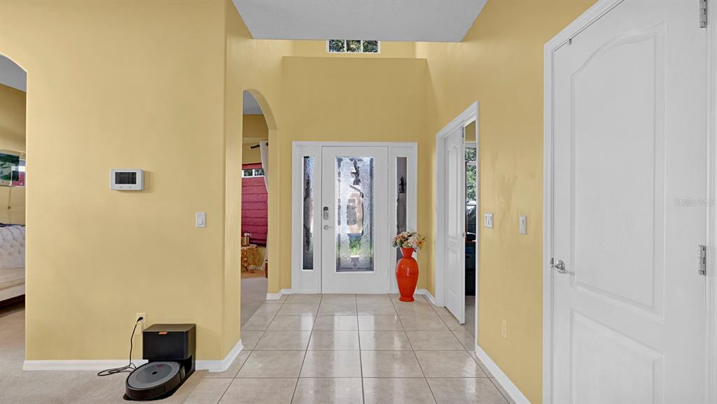 A bright entryway features yellow walls, tile flooring, a glass-paneled front door, and high ceilings — 3295 SAFE HARBOR LANE, LAKE MARY, FL