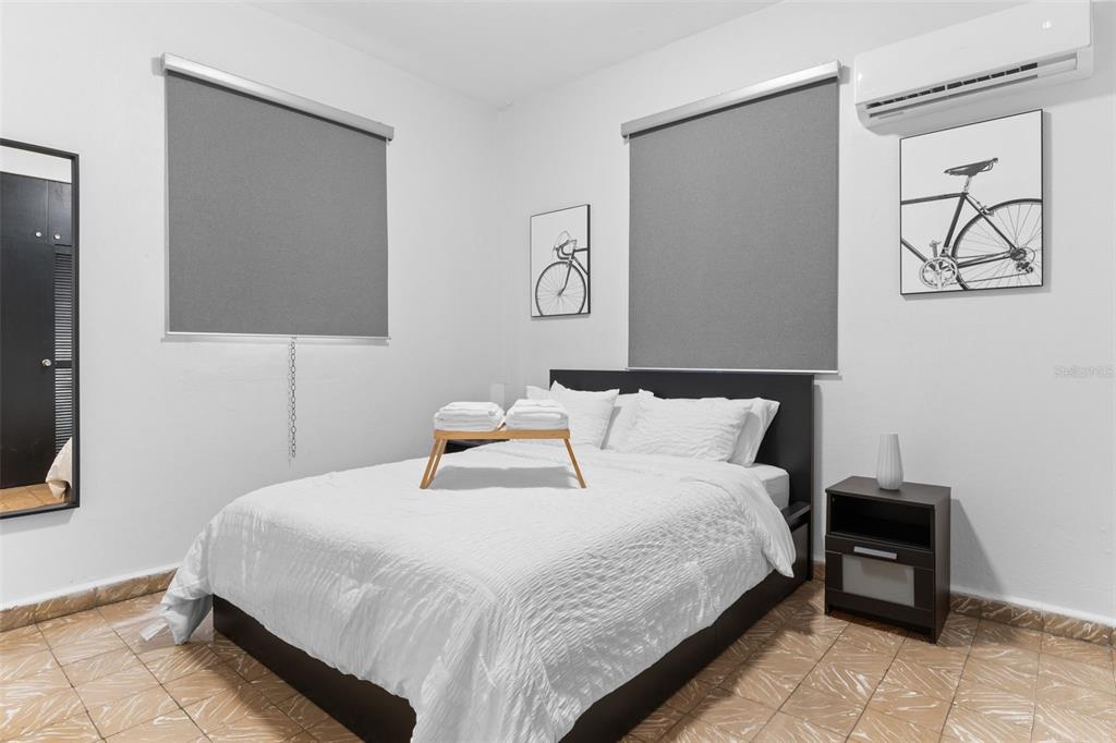 A bedroom features a bed with white linens, two windows with grey shades, and tile flooring — 261 DUFFAUNT, SAN JUAN, PR