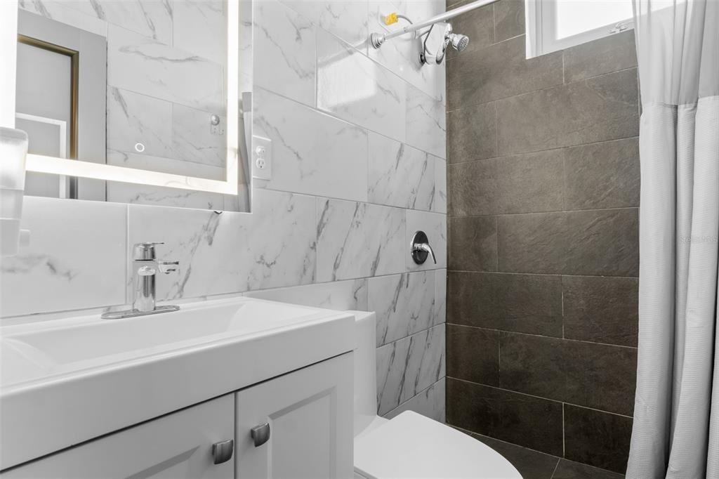 A modern bathroom features a white vanity, marble-look wall tiles, and a dark tiled shower — 261 DUFFAUNT, SAN JUAN, PR