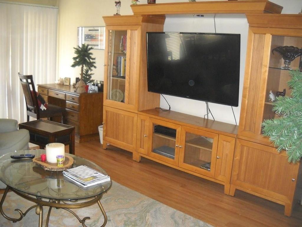 A living room features a large wooden entertainment center, a glass-topped coffee table, and wood flooring — 3471 CLARK ROAD UNIT 269, SARASOTA, FL
