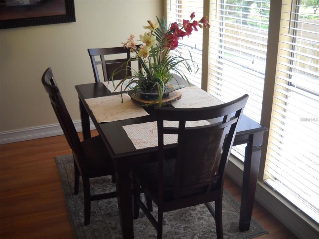 A dark wood dining table with four chairs sits on a rug near large windows — 3471 CLARK ROAD UNIT 269, SARASOTA, FL