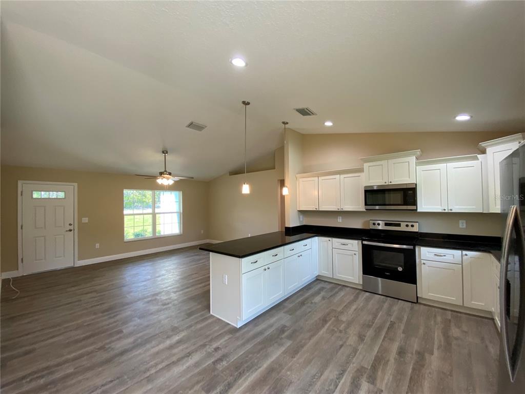 An open-concept kitchen with white cabinets, black countertops, and wood-look flooring — 2810 W PINTADO DRIVE, DUNNELLON, FL