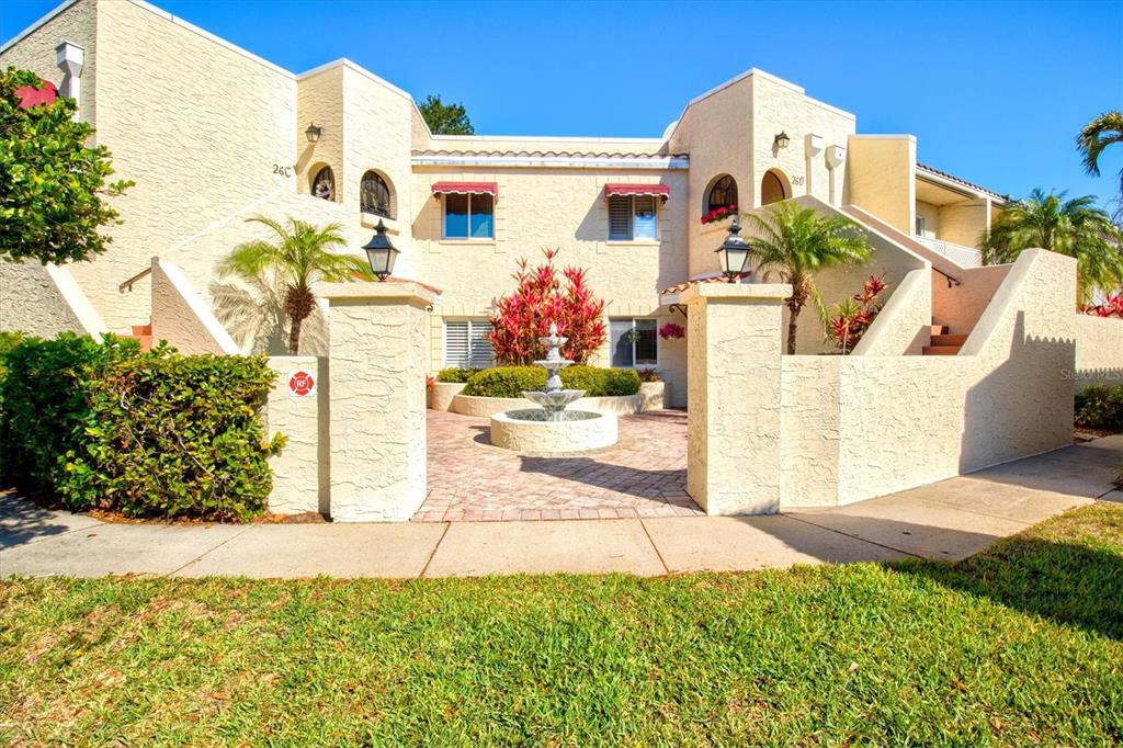 A two-story stucco apartment building features a central courtyard with a fountain and landscaping — 6101 34TH STREET W UNIT 26C, BRADENTON, FL