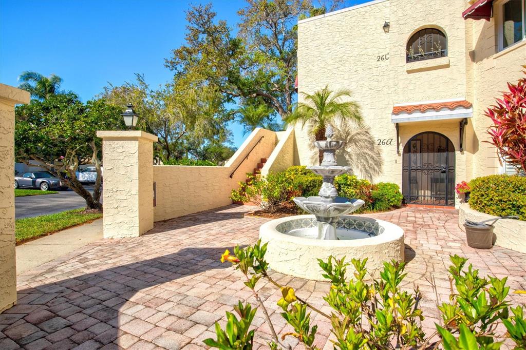 A stone fountain sits on a brick patio in front of a stucco building exterior — 6101 34TH STREET W UNIT 26C, BRADENTON, FL