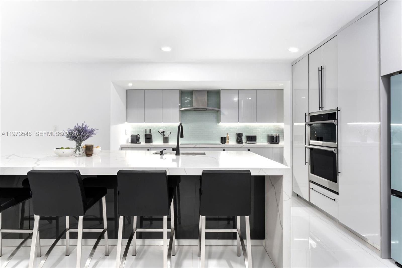 A modern kitchen features a white marble island, dark cabinetry, and built-in stainless steel appliances — 400 SW 24th Rd, Miami FL 33129, MIAMI, FL