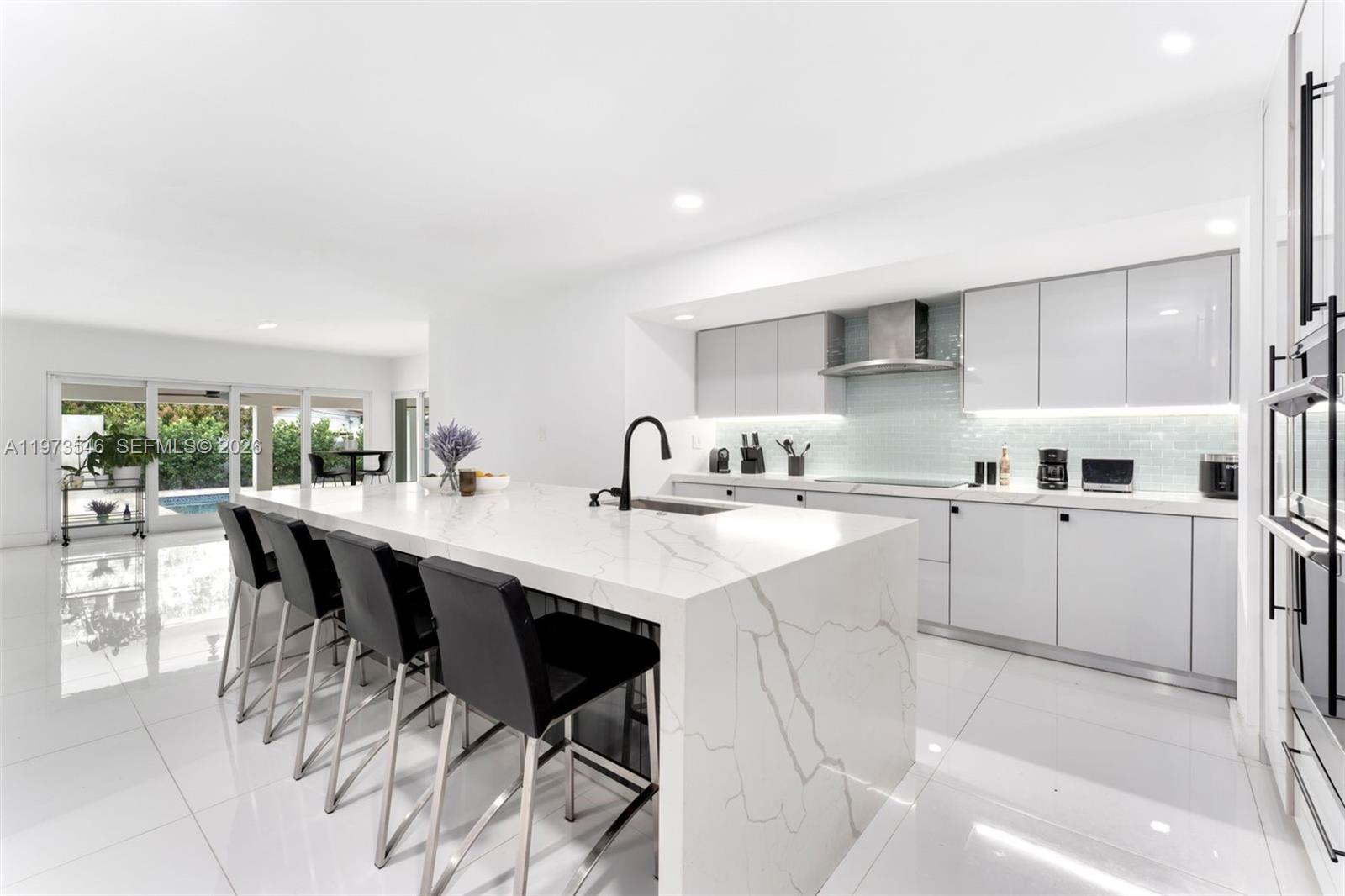A modern kitchen features a large marble waterfall island with black stools and white cabinetry — 400 SW 24th Rd, Miami FL 33129, MIAMI, FL