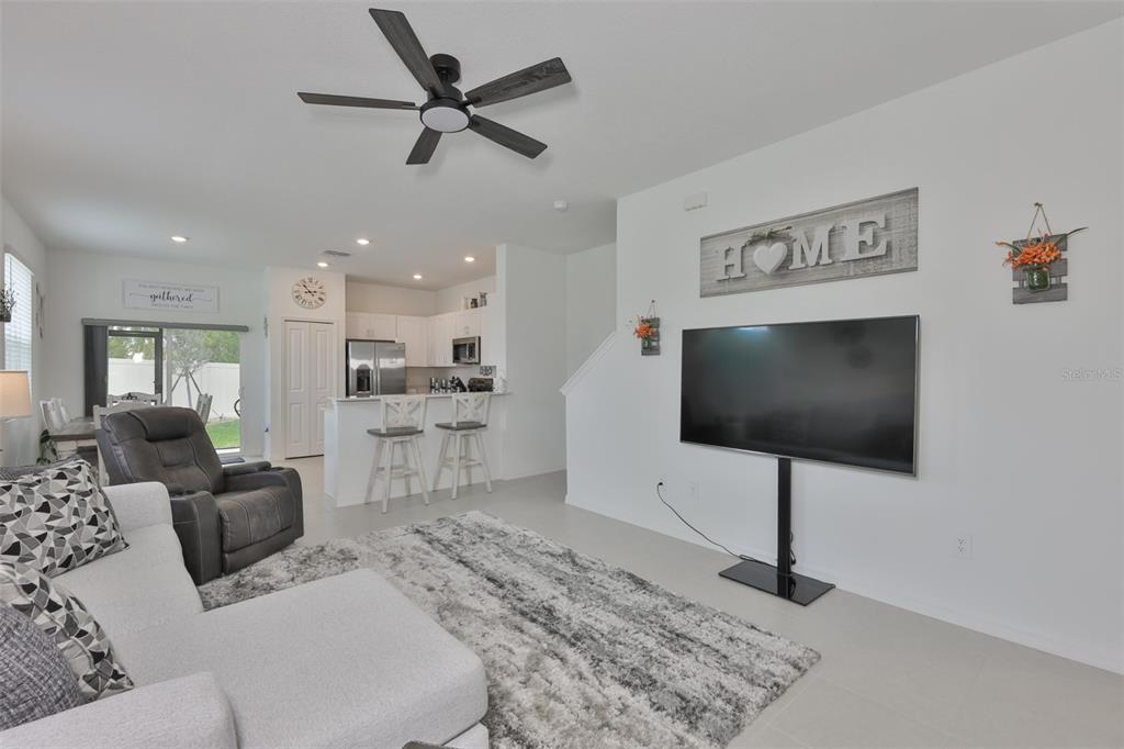 A living room features a gray sectional, a wall-mounted television, and an open-concept kitchen — 2661 SUNRAY VENUS WAY, RUSKIN, FL