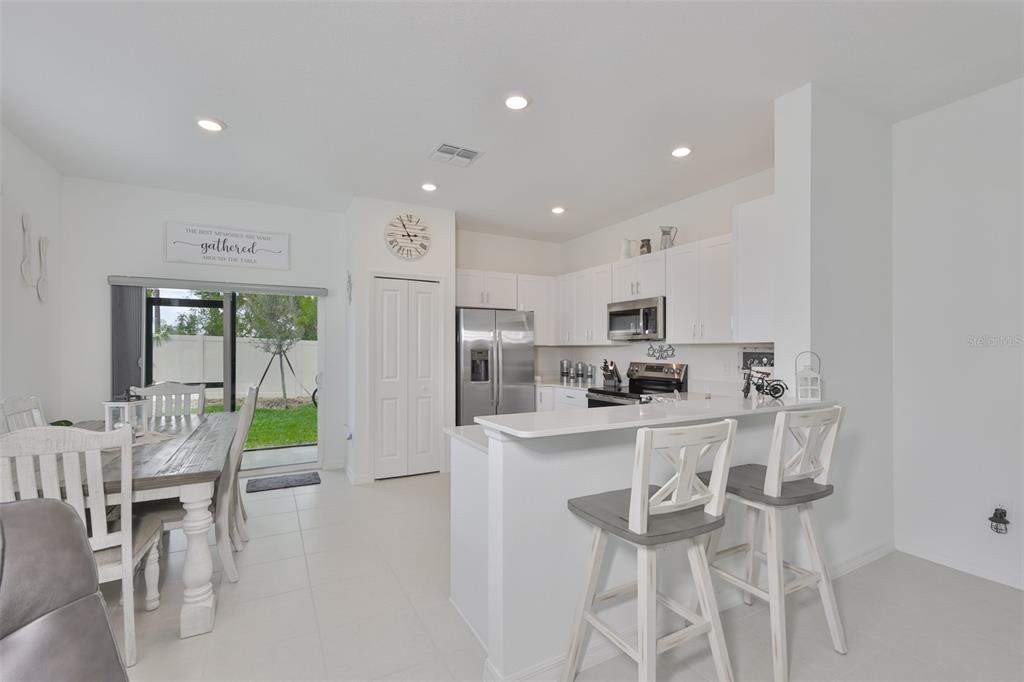 A bright kitchen and dining area features white cabinets, stainless steel appliances, and bar seating — 2661 SUNRAY VENUS WAY, RUSKIN, FL