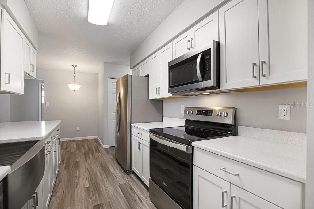 A galley kitchen features white cabinets, stainless steel appliances, and light-colored countertops — 423 VAN REED MANOR DRIVE, BRANDON, FL