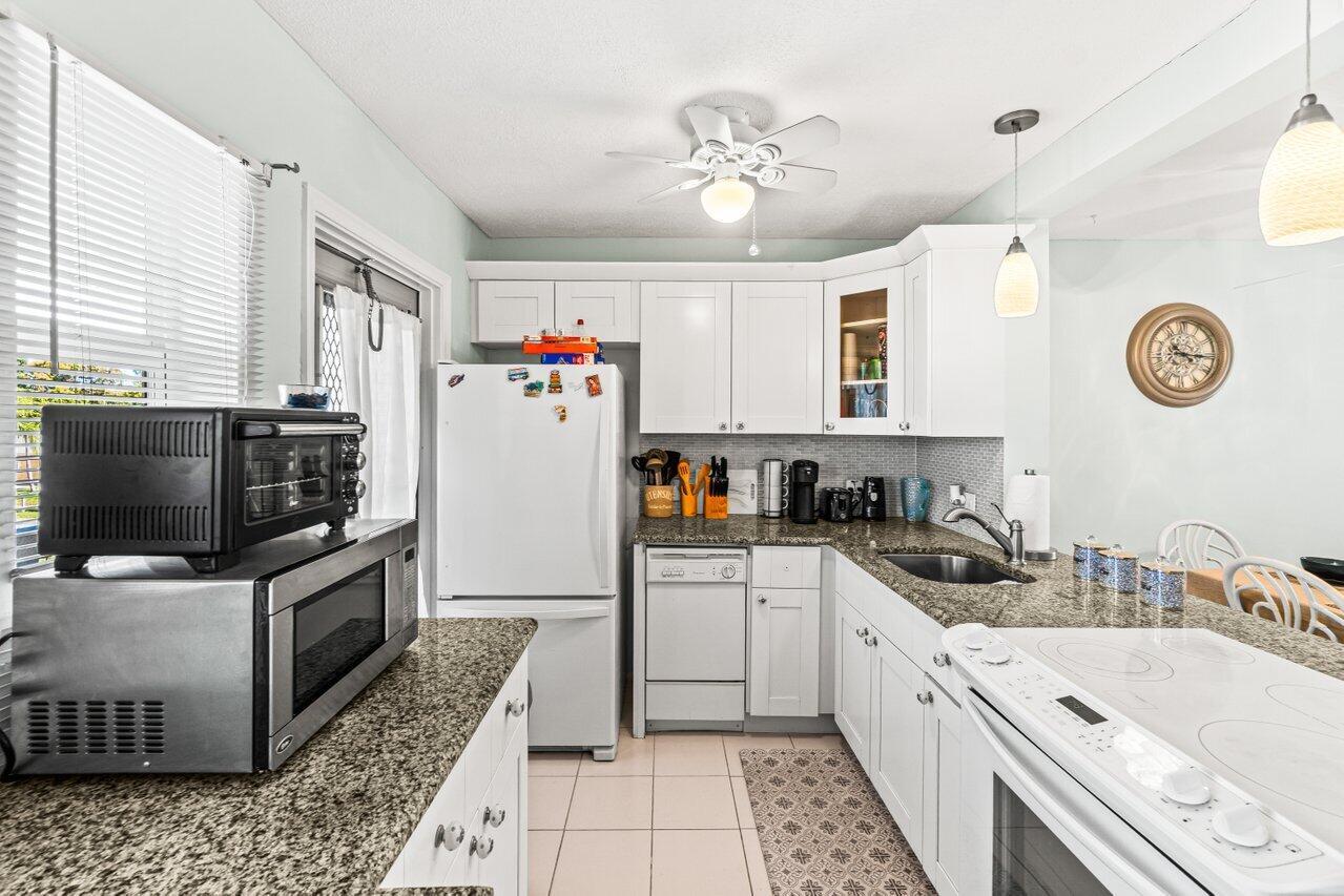 A kitchen features white cabinets, granite countertops, stainless steel appliances, and a tiled floor — 2121 NE 1st Court # 202, Boynton Beach FL 33435, BOYNTON BEACH, FL