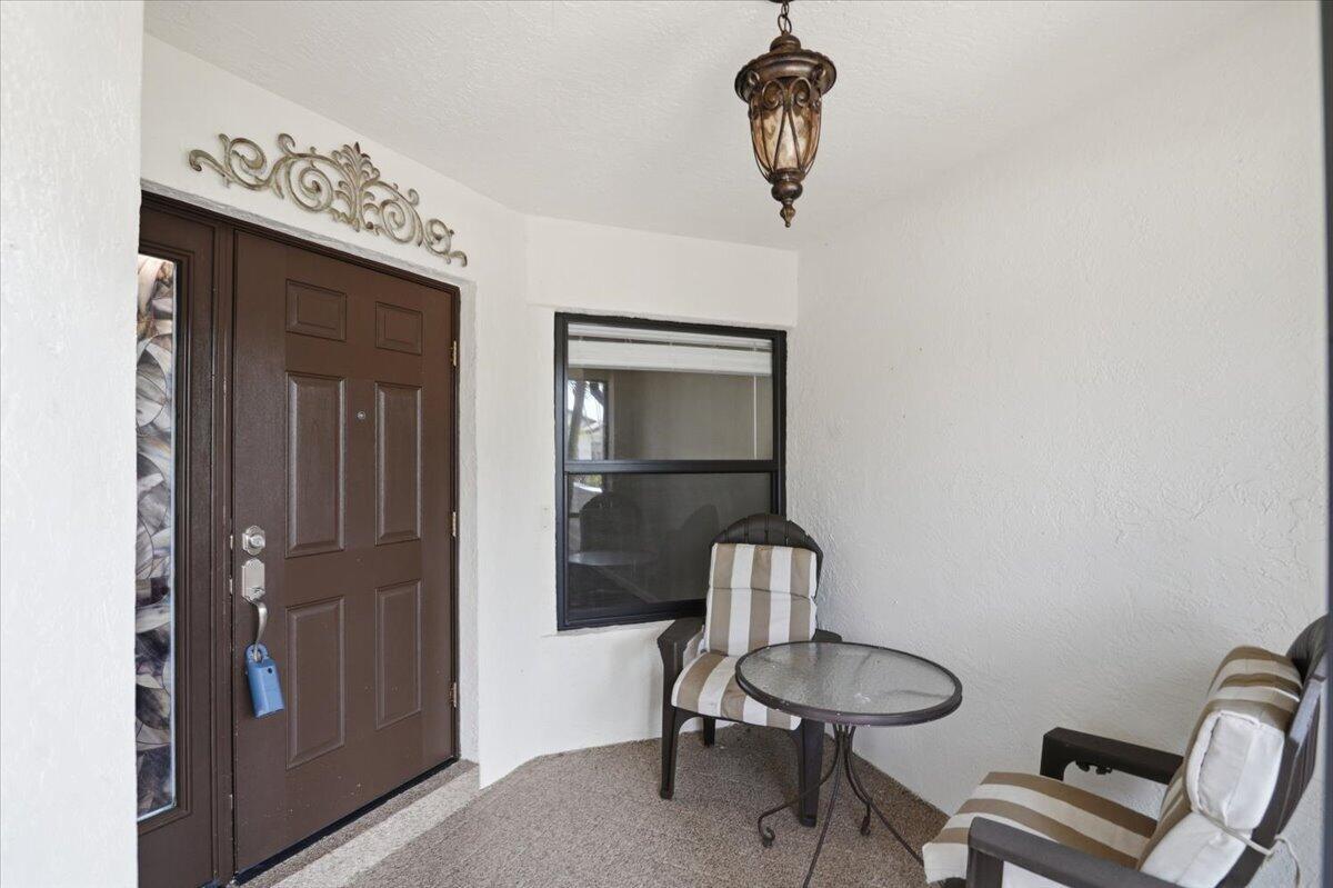 A covered entryway features a brown front door, a small bistro set, and a hanging lantern — 21583 Villa Nova Drive, Boca Raton FL 33433, BOCA RATON, FL