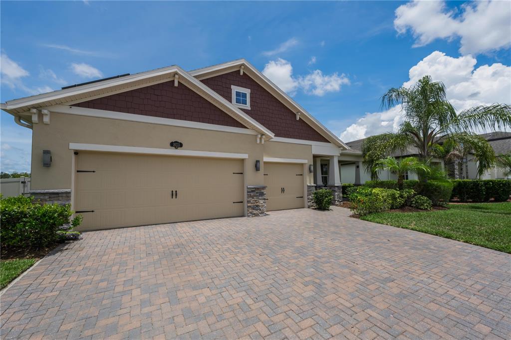 A tan house with a three-car garage and a paved driveway under a blue sky — 18233 ROSEATE DRIVE, LUTZ, FL