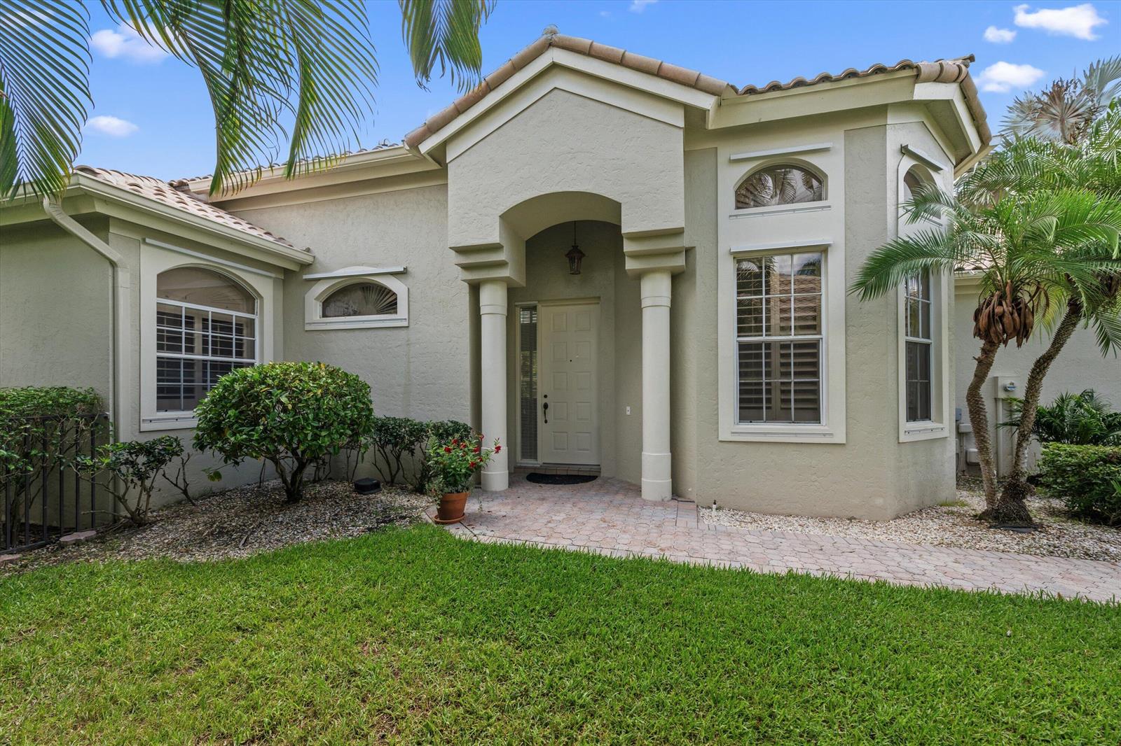 The exterior of a beige stucco house features a covered entryway with two white columns — 12557 Mallet Circle, Wellington FL 33414, WELLINGTON, FL