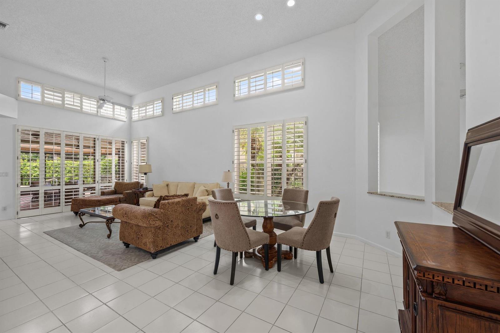 A bright, high-ceilinged living and dining area features white tile floors and plantation shutters — 12557 Mallet Circle, Wellington FL 33414, WELLINGTON, FL